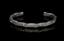 Textured silver cuff bracelet with twisted design and golden spherical studs, reflecting on a black surface.