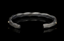 Dark grey twisted metal cuff bracelet with hammered textured ends, golden accent beads, and 'Wd 18K 925' stamps visible inside.