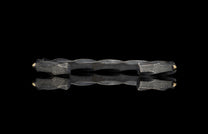 Dark twisted metal bracelet with hammered ends and gold spheres, shown with a reflection.