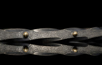 Dark hammered metal bracelet featuring gold spherical rivets and an intertwined design.