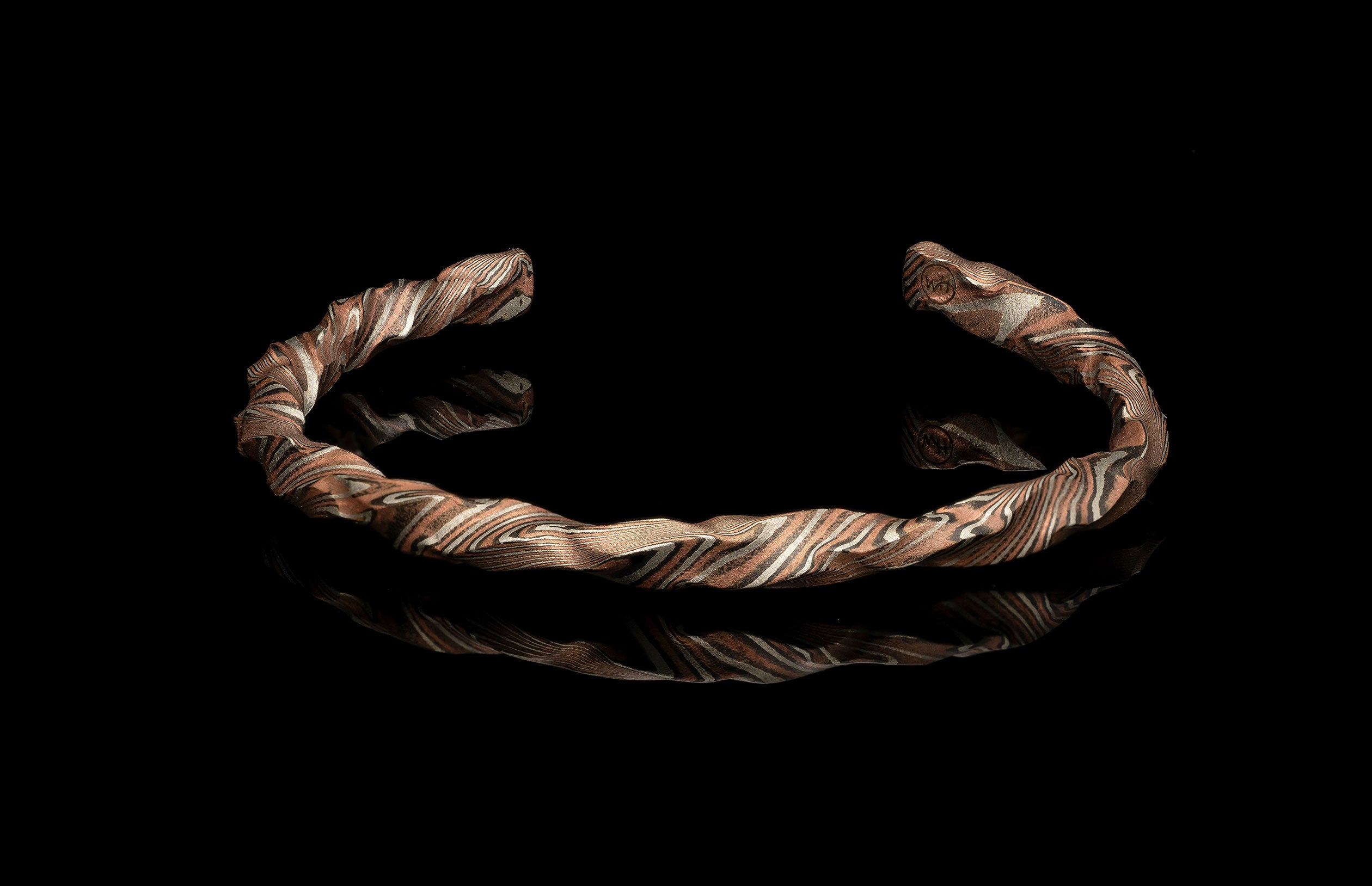 Twisted copper and silver-toned layered cuff bracelet on a reflective black surface.