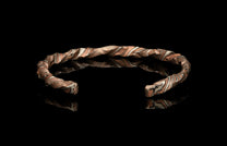 Multi-toned metallic cuff bracelet with wavy copper and silver "strata" pattern, shown on a reflective surface.