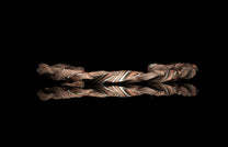 Coppery and silver-striped metallic bracelet featuring a layered strata pattern, reflected on black.