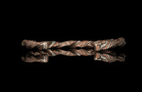 Twisted multi-toned metal bracelet with brown, silver, and black layered patterns, reflected on a black surface.