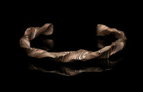 Wavy layered metal cuff bracelet featuring swirling copper-brown and silver-white patterns, reflecting on a black surface.