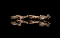 Wavy patterned jewelry piece with copper and silver stripes on a reflective black surface.