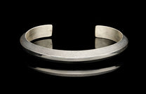 Silver cuff bracelet with a hammered texture on its upper band and a polished lower band, on a reflective black surface.