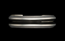 Silver cuff bracelet with a textured dark gray surface, smooth silver bands, and tapered edges, reflected on black.