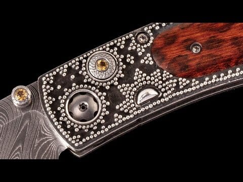 Ornate folding knife with a Damascus blade, silver-dotted dark metal handle, golden gems, and a reddish-brown wood inlay.