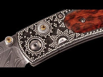 Ornate folding knife with a Damascus blade, silver-dotted dark metal handle, golden gems, and a reddish-brown wood inlay.