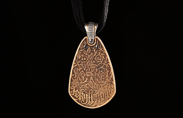 Bronze teardrop pendant with intricate embossed leaves, vines, and "Jekyll + Hyde" text, on a black cord.