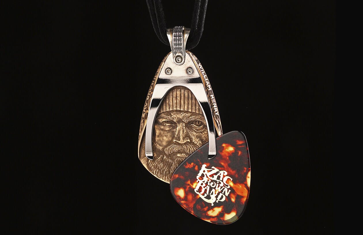 Bronze and silver-toned pendant by William Henry, featuring a carved bearded man's face and holding a tortoiseshell guitar pick.