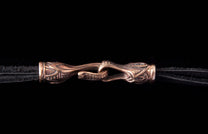 Bronze hook-and-eye clasp by Jekyll + Hyde, featuring an ornate, mythical design, connecting two black cords.