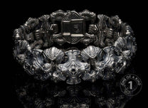 Silver-toned metal bracelet with intricate, ornate skull-like and armored links, detailed engravings, on a reflective black surface.