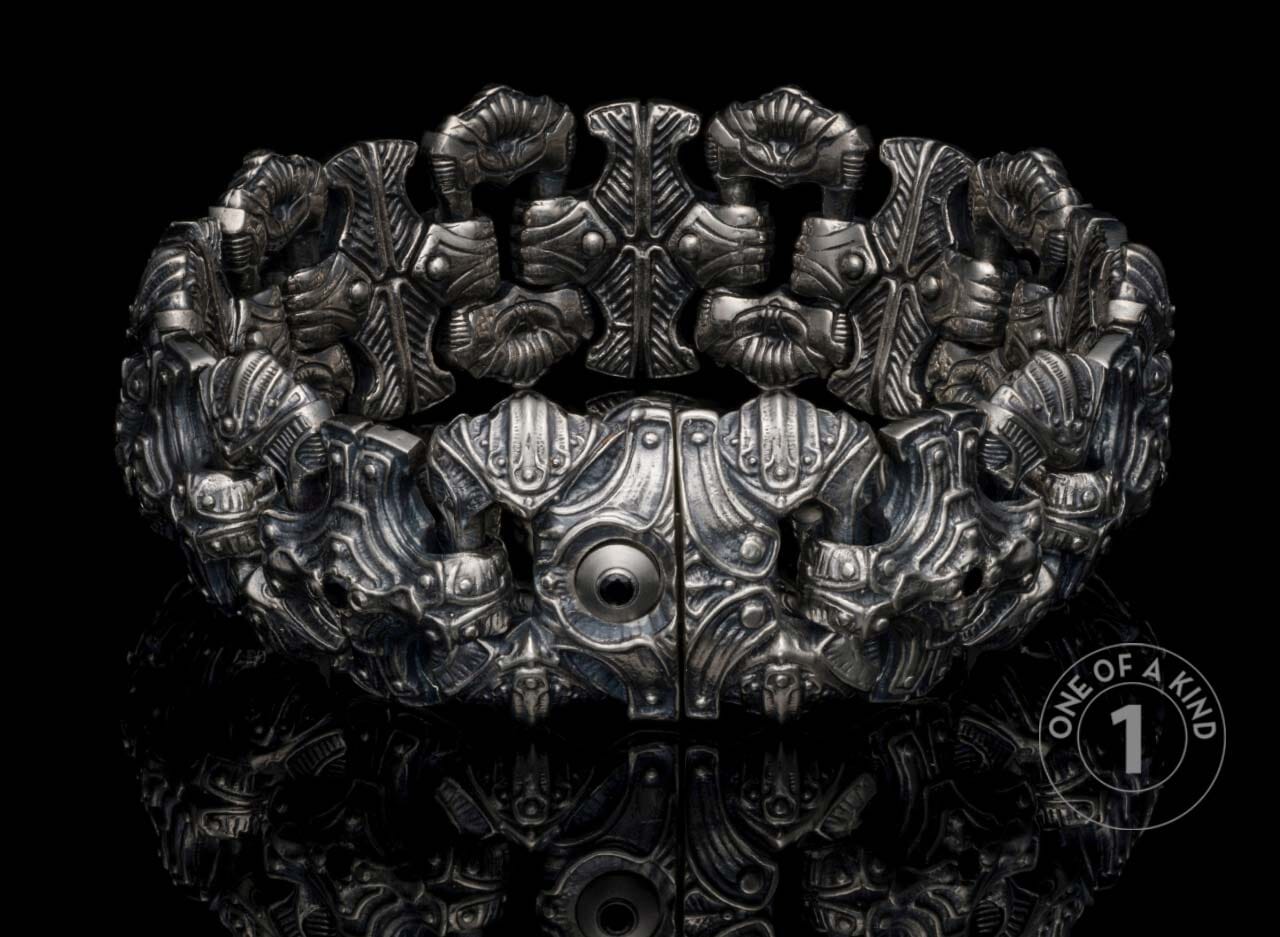 Intricate silver-toned bracelet featuring sculptural, mechanical designs and a central dark accent.