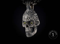 Ornate silver skull pendant with intricate tribal carvings, green gemstone eyes, hanging from a metal chain.