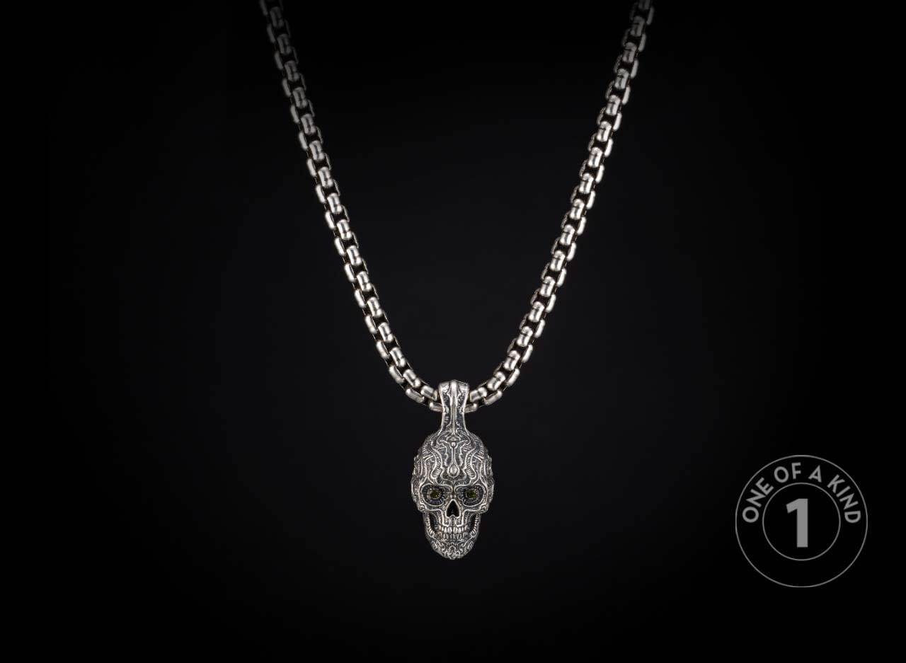 Intricate silver skull pendant necklace with dark eyes on a thick box chain, hanging vertically.