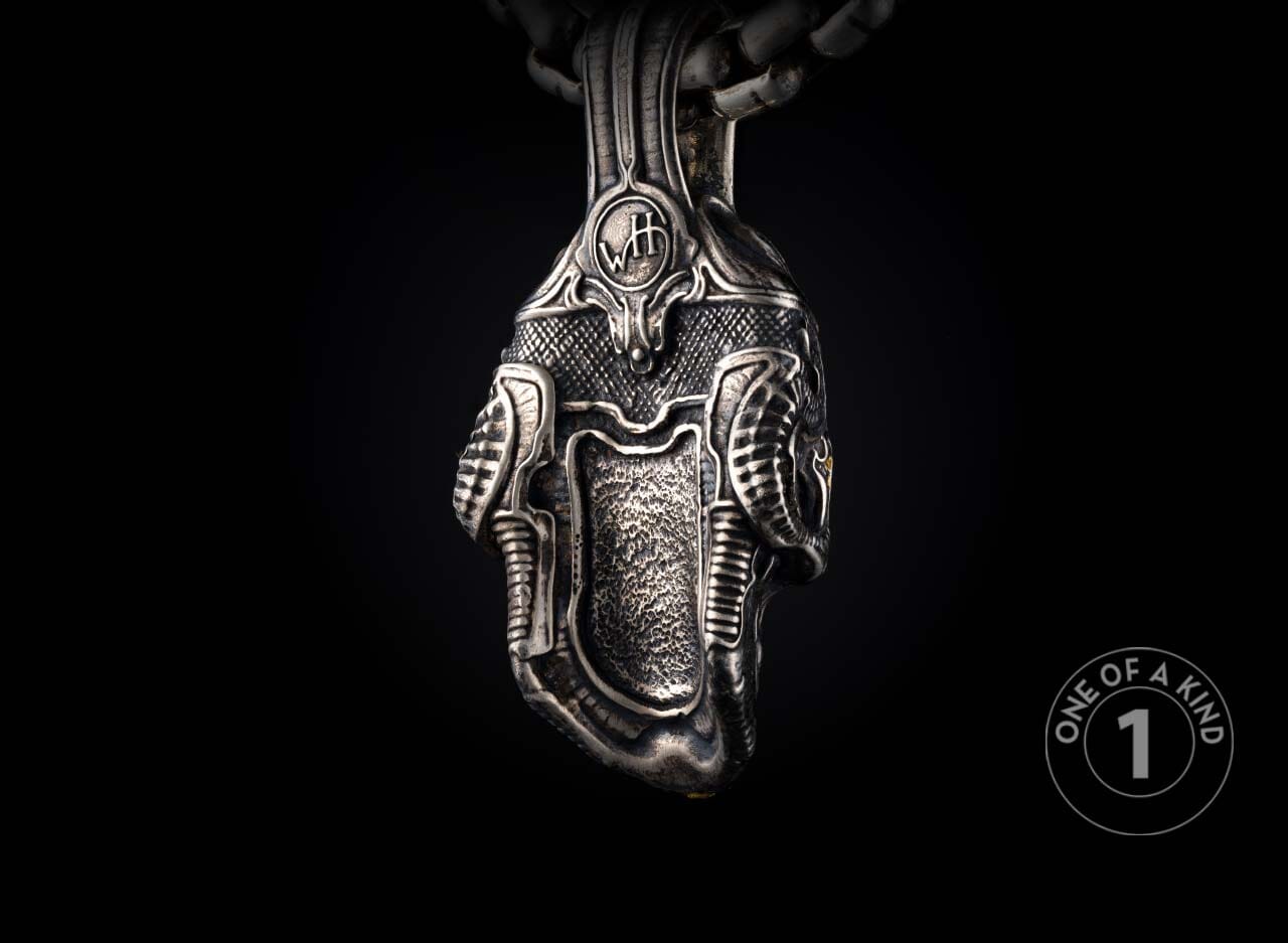 Intricate silver pendant with textured surface, featuring a central panel, ridged sides, and a 'WH' emblem.