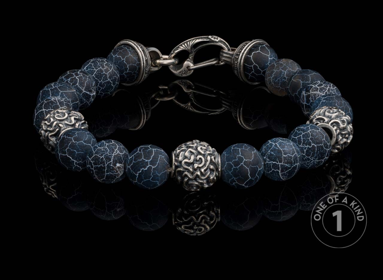 Sterling silver beaded bracelet with dark blue crackle agate beads and ornate silver accent beads, on a reflective surface.