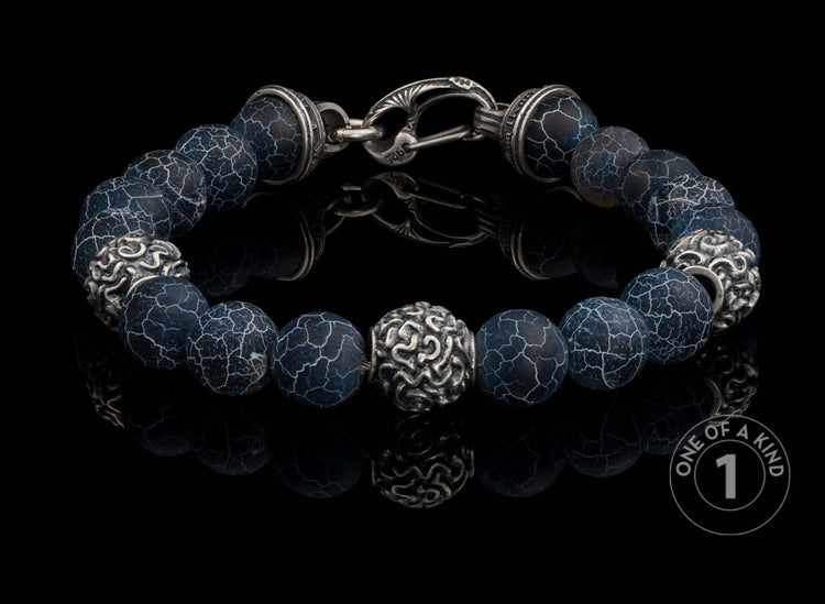 Sterling silver beaded bracelet with dark blue crackle agate beads and ornate silver accent beads, on a reflective surface.