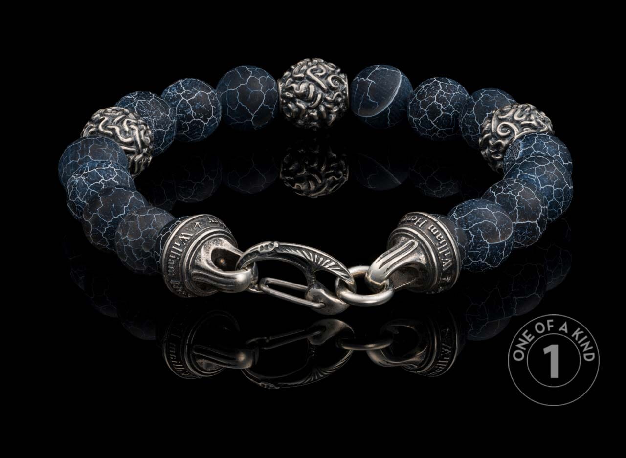 Dark blue cracked agate beaded bracelet with ornate silver-toned accents, a decorative clasp engraved 'William Henry', and reflected on a black surface.