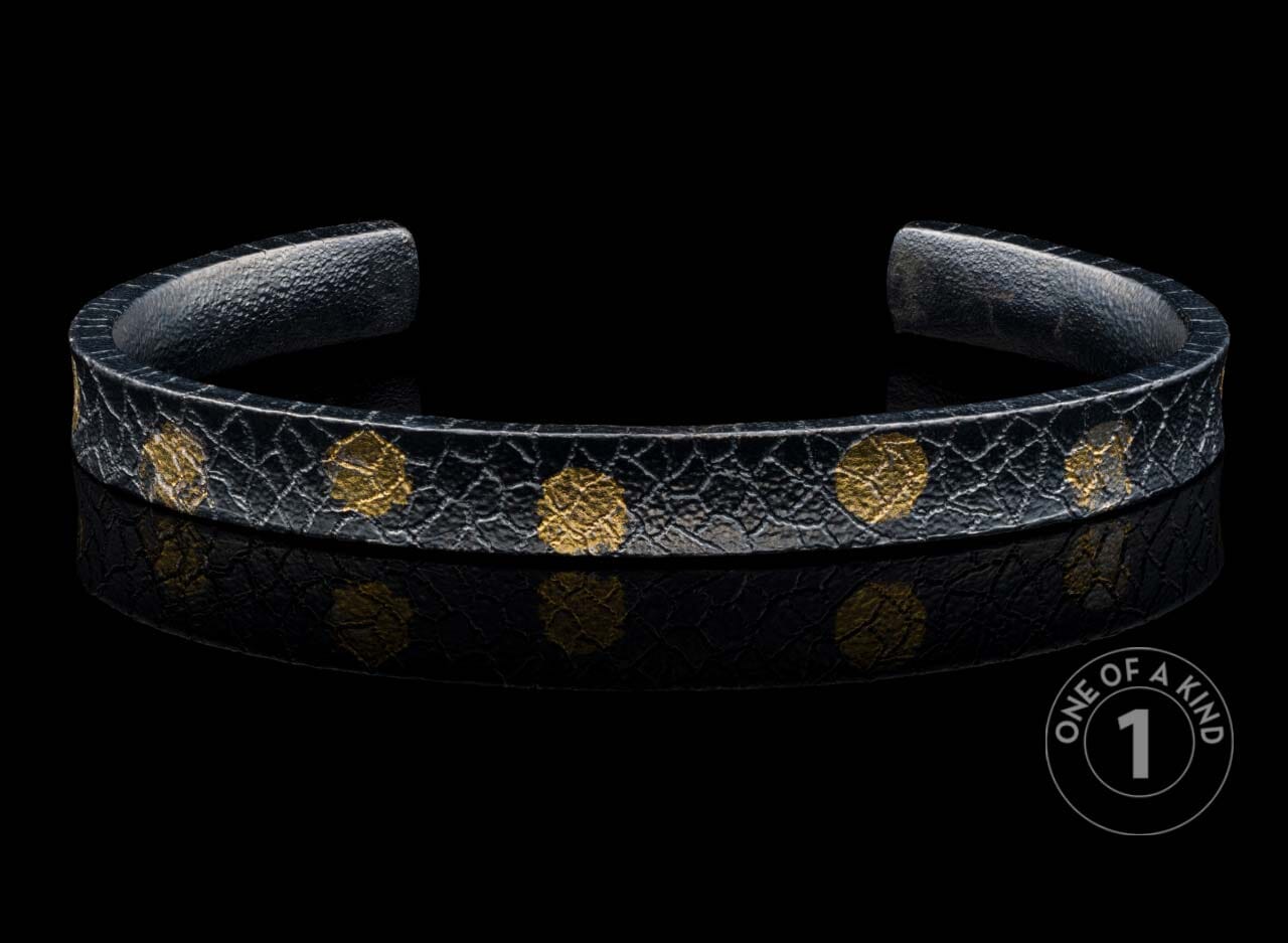 Black textured cuff bracelet with scattered gold-colored organic patterns.