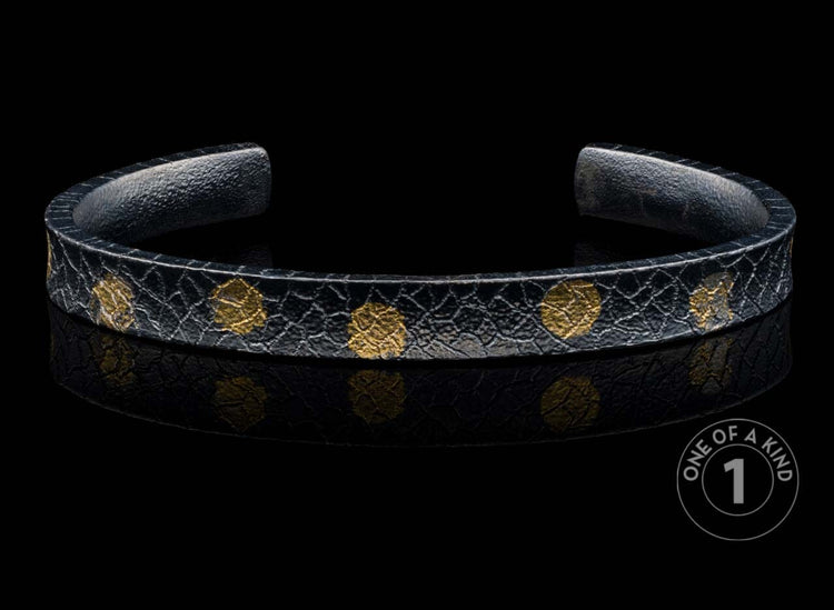 Black textured cuff bracelet with scattered gold-colored organic patterns.