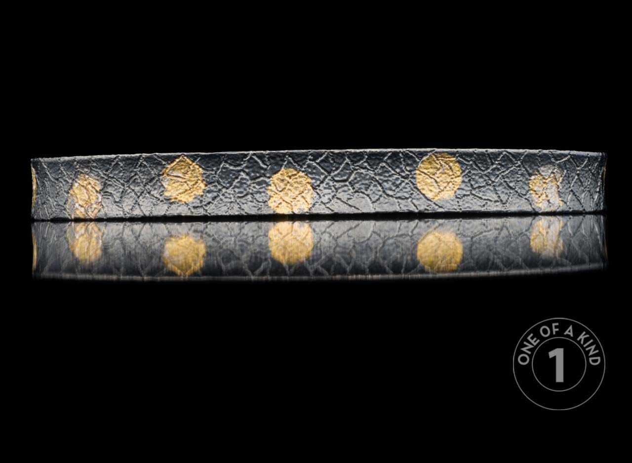 Dark textured bracelet with crinkled gold circular patterns reflected on black.