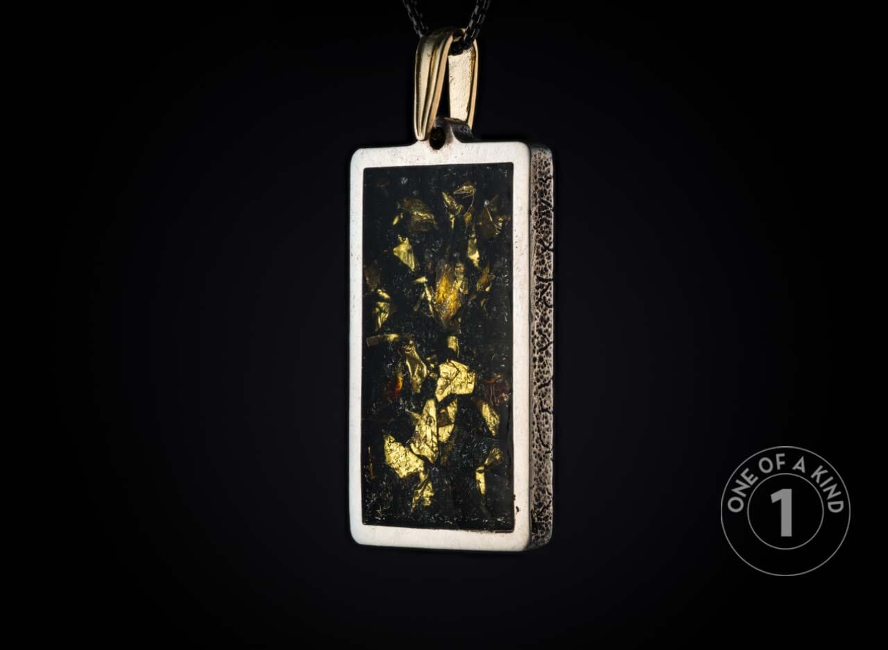 Rectangular silver-toned pendant with a dark center filled with glistening gold flakes, featuring textured sides and a gold bail, suspended against a black background.
