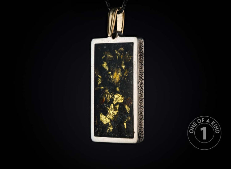 Rectangular silver-toned pendant with a dark center filled with glistening gold flakes, featuring textured sides and a gold bail, suspended against a black background.