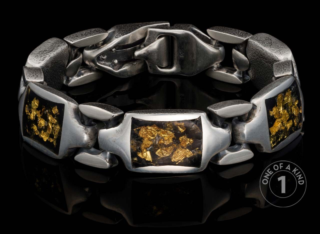 Chunky oxidized silver link bracelet with rectangular inlays of dark material speckled with gold flakes, on a reflective black surface.