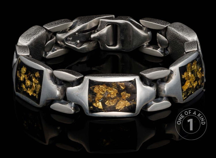 Chunky oxidized silver link bracelet with rectangular inlays of dark material speckled with gold flakes, on a reflective black surface.