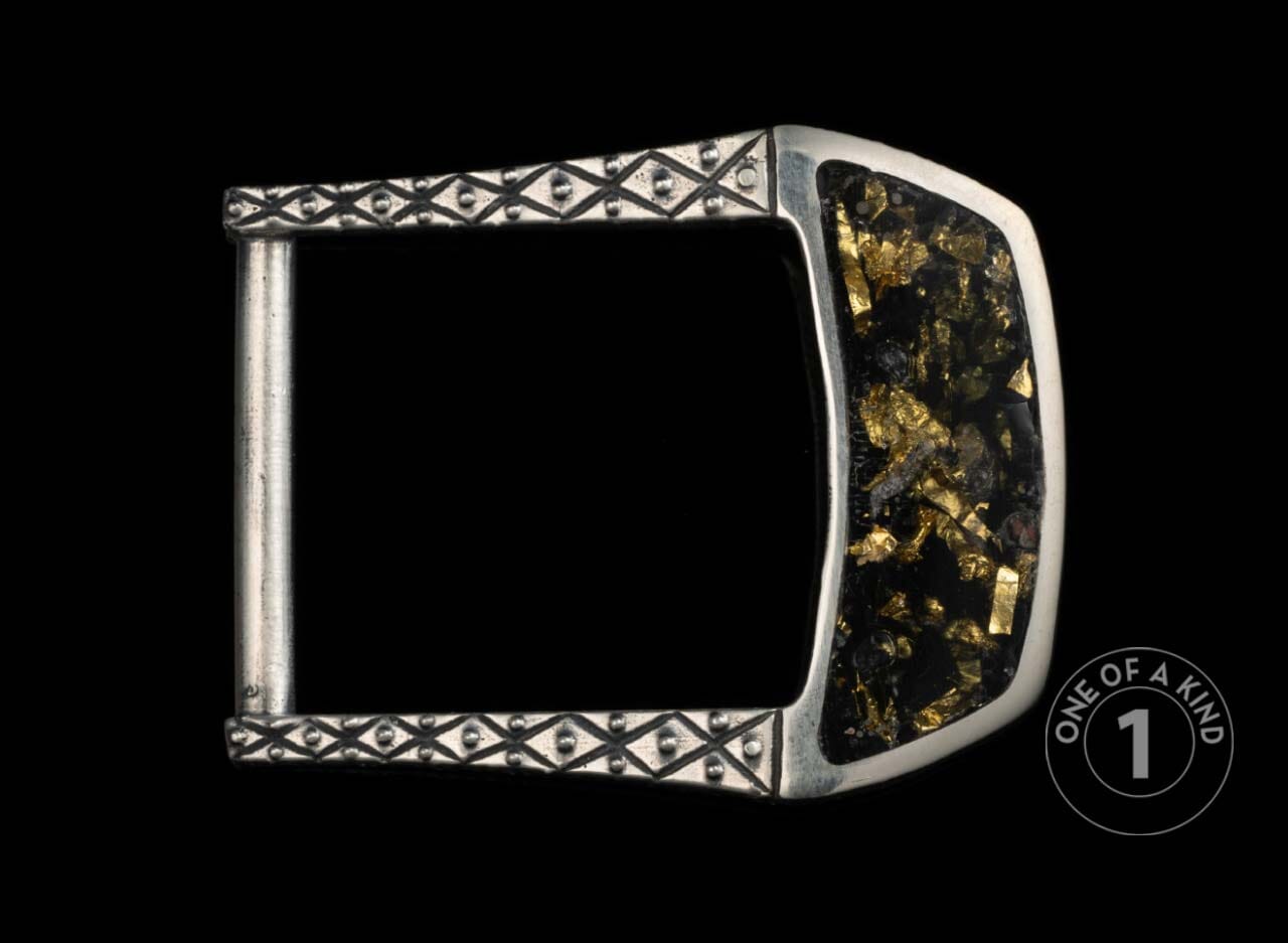 Silver metal belt buckle with black and gold flake inlay, featuring an ornate diamond pattern and 'one of a kind' mark.