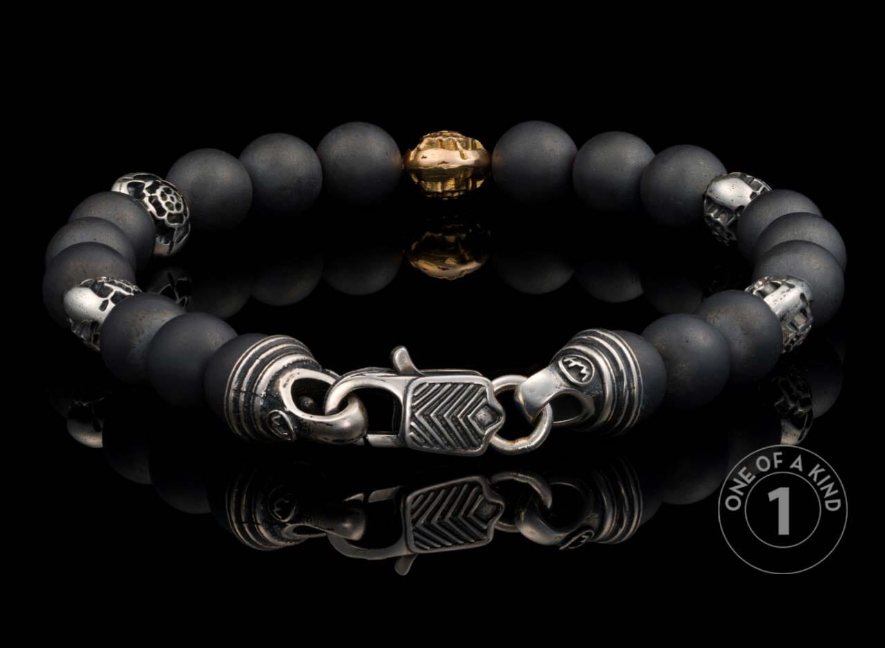 Matte black beaded bracelet with a central gold bead, intricate silver skull and patterned spacers, and a detailed silver clasp.