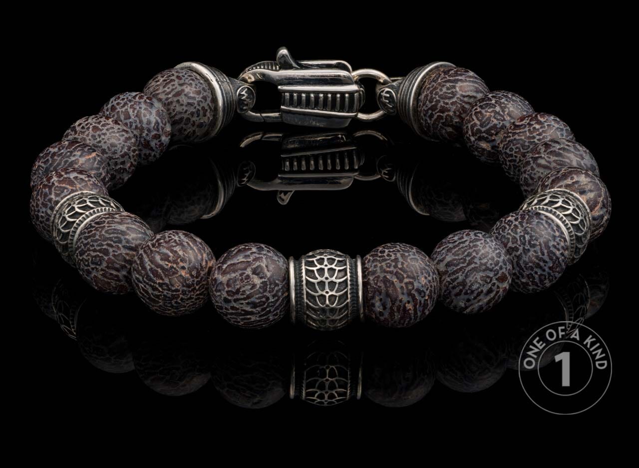 Dark patterned beaded bracelet with intricate silver spacers and a unique clasp, reflected on a black surface.
