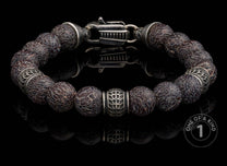 Dark patterned beaded bracelet with intricate silver spacers and a unique clasp, reflected on a black surface.