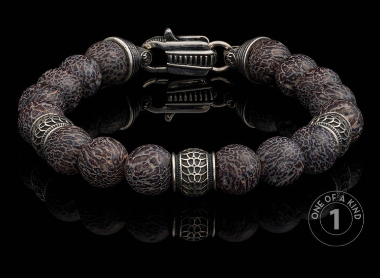 Dark patterned beaded bracelet with intricate silver spacers and a unique clasp, reflected on a black surface.
