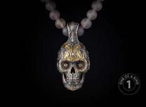 Ornate silver and gold skull pendant with intricate carvings and dark gemstone eyes, suspended from a translucent beaded necklace.