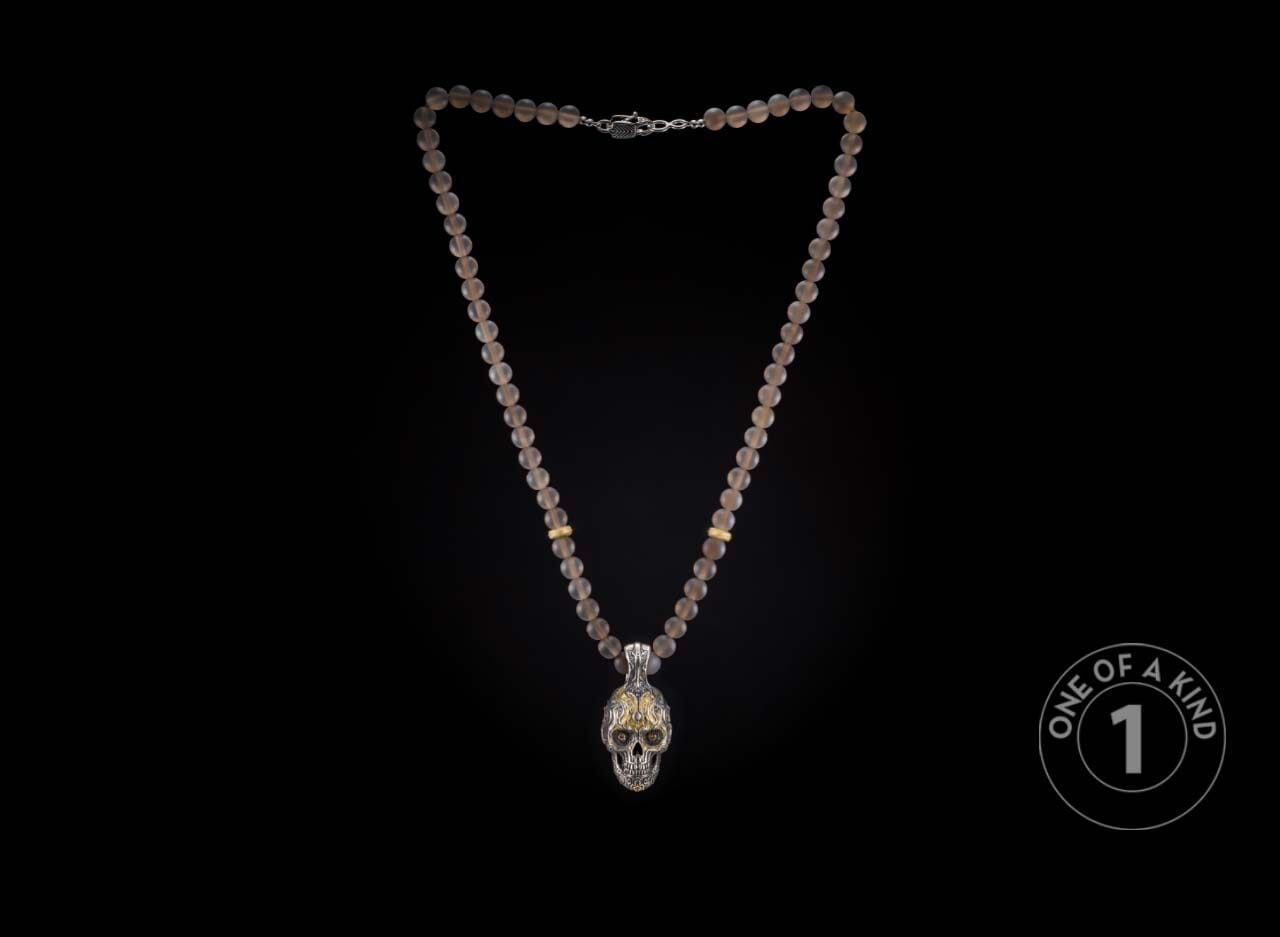 Translucent grey beaded necklace with a detailed silver skull pendant and gold accents.