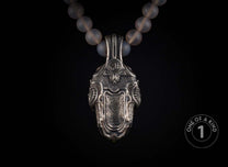 Ornate silver-toned pendant with a 'WH' monogram, featuring a textured design and paired with a frosted bead necklace.