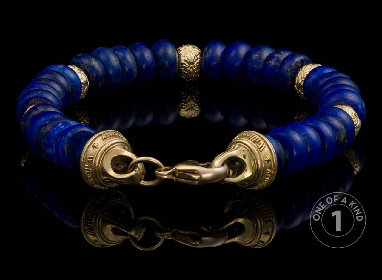 Blue lapis lazuli beaded bracelet with gold lion head bead, gold spacers, and a gold lobster clasp, reflected.
