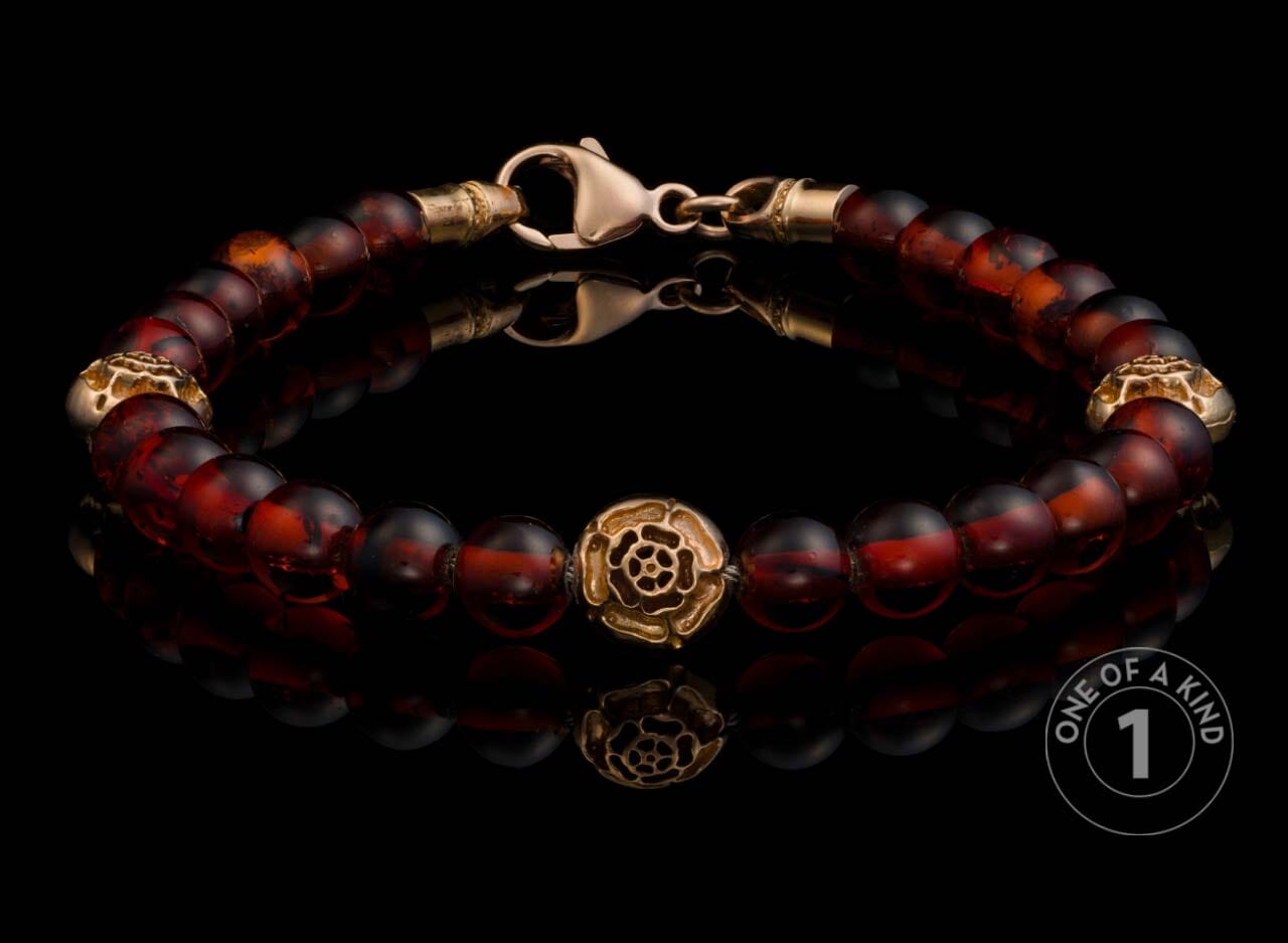 Amber beaded bracelet featuring a gold rose center bead and textured gold accents, presented on a reflective surface.