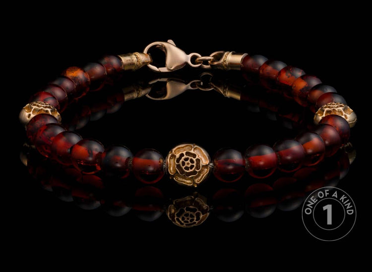 Amber beaded bracelet featuring a gold rose center bead and textured gold accents, presented on a reflective surface.
