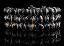Chunky multi-strand bracelet with polished black and white marbled beads and silver-toned links, displayed with reflection.