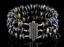 Three-strand bracelet with black, white, and tan banded agate beads and a silver-toned clasp, on a reflective black surface.