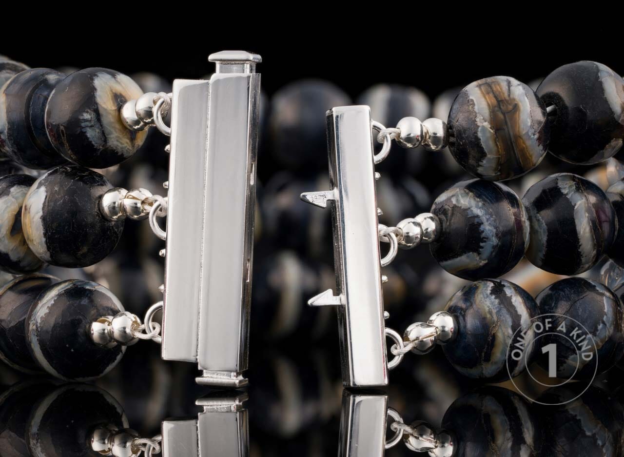 Multi-strand beaded bracelet with swirling black, white, brown, and grey beads and an open silver-tone box clasp.