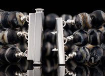 Multi-strand beaded bracelet with swirling black, white, brown, and grey beads and an open silver-tone box clasp.