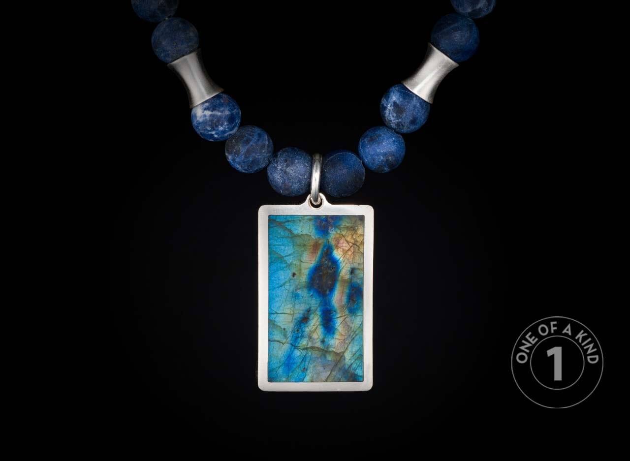 Blue beaded necklace with silver spacers and a rectangular pendant featuring an iridescent blue, green, and gold gemstone.