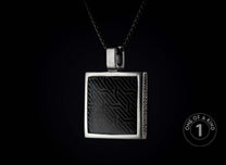 Square silver-toned metal pendant with a black insert featuring a wavy geometric pattern and textured sides, hanging from a dark chain.
