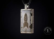 Oxidized silver rectangular pendant featuring an engraved rocket, stars, and textured frame on a dark chain.